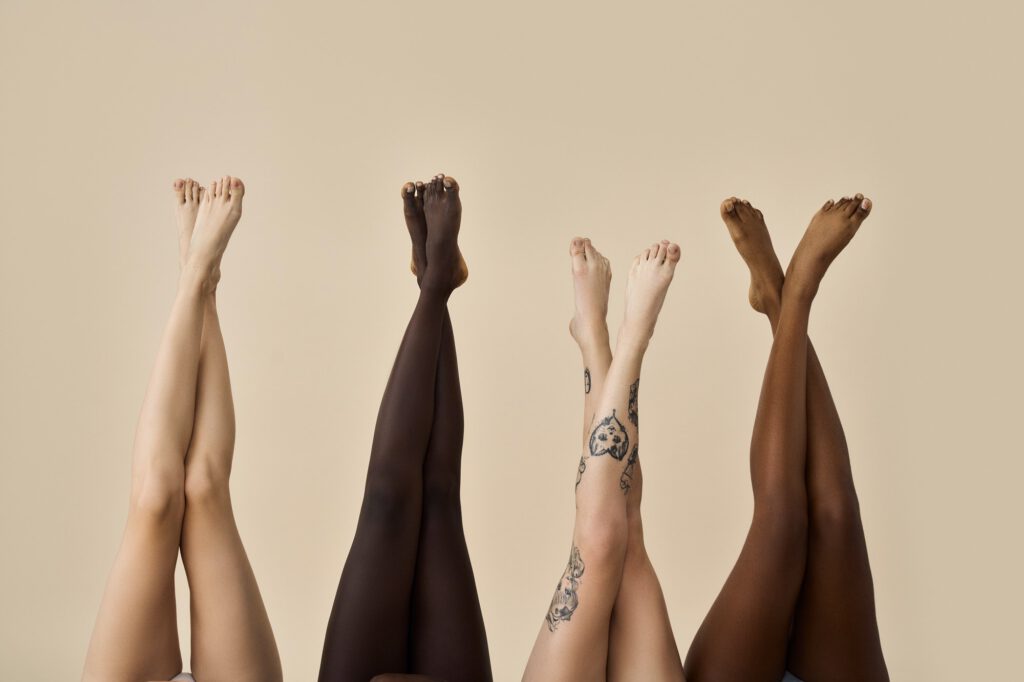 Diverse female legs raised up on beige background. Hair removal concept.