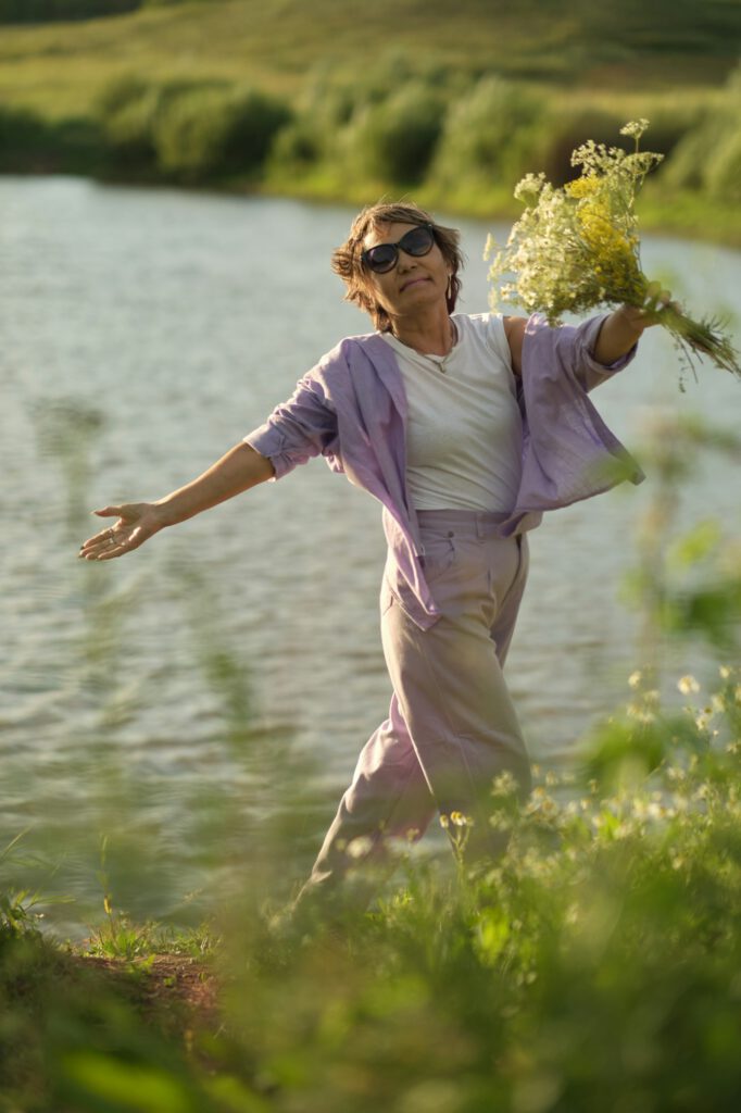 Amidst gentle waters, the mature Asian woman stands with a bouquet, her stance a meditative harmony
