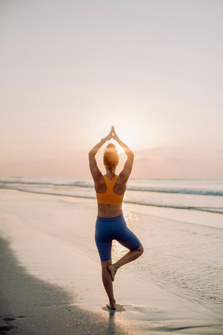 Rear view of young woman taking exercises at beach, morning routine and healthy lifestyle concept.