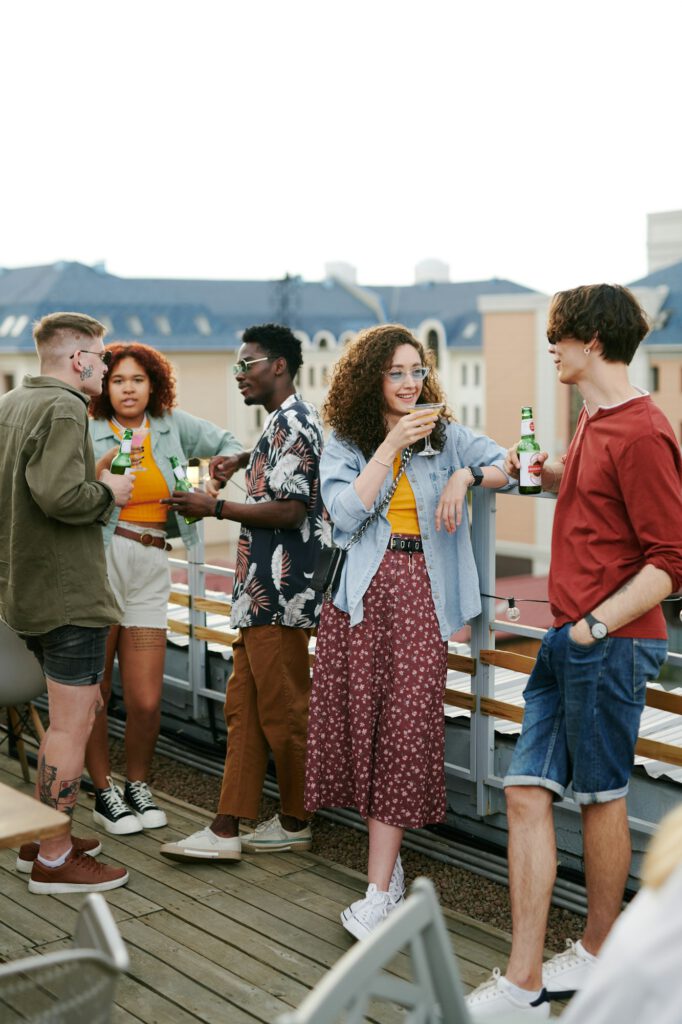 Young couple with drinks having chat against group of their friends at party