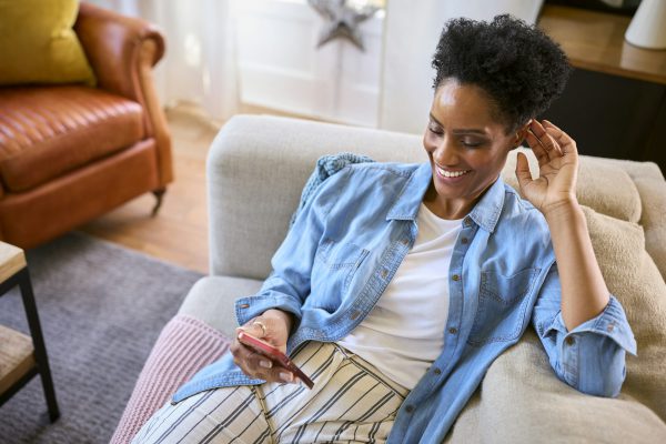Mature Woman Relaxing On Sofa At Home Looking At Mobile Phone